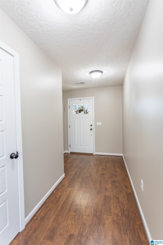 hall with dark wood-style flooring, a textured ceiling, and baseboards