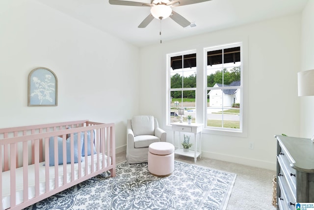 carpeted bedroom with ceiling fan and a crib