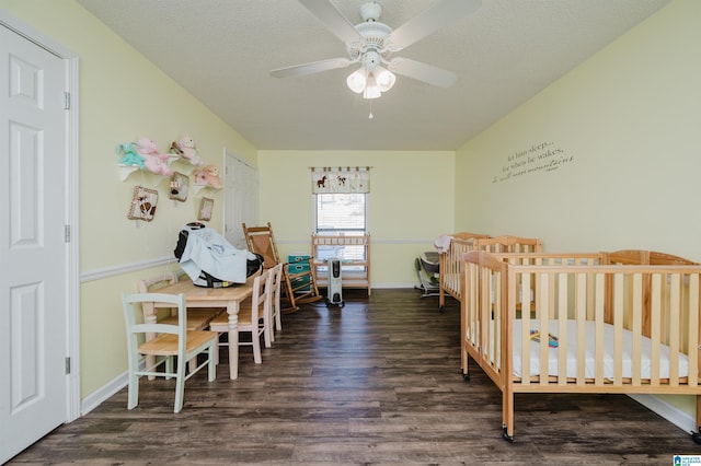 bedroom with ceiling fan, a nursery area, dark wood-type flooring, and a textured ceiling