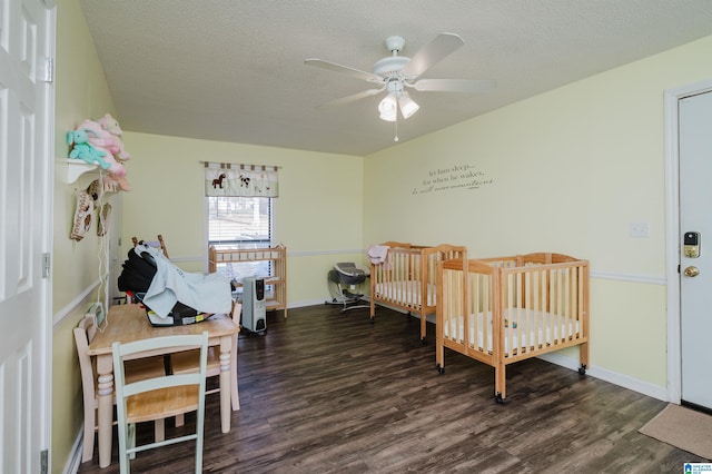 bedroom featuring dark wood-type flooring, ceiling fan, a textured ceiling, and a nursery area