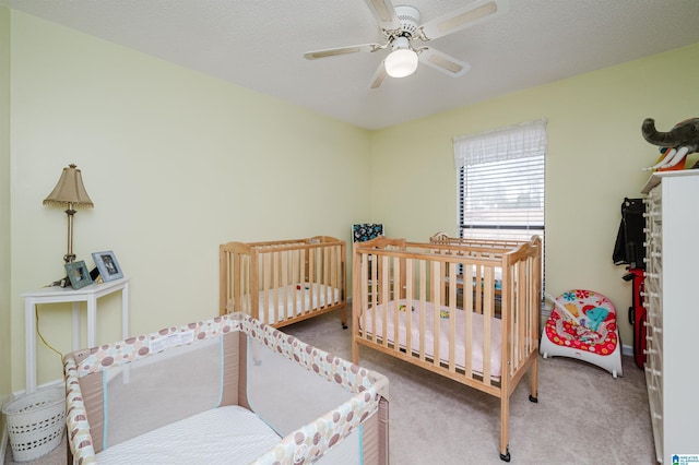 bedroom with ceiling fan, carpet, a nursery area, and a textured ceiling