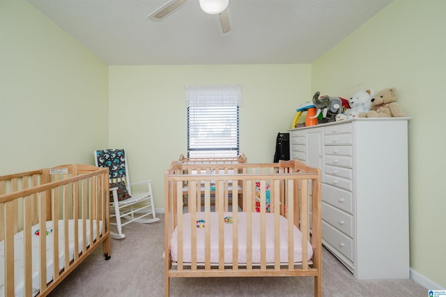 bedroom featuring ceiling fan, light colored carpet, a textured ceiling, and a crib