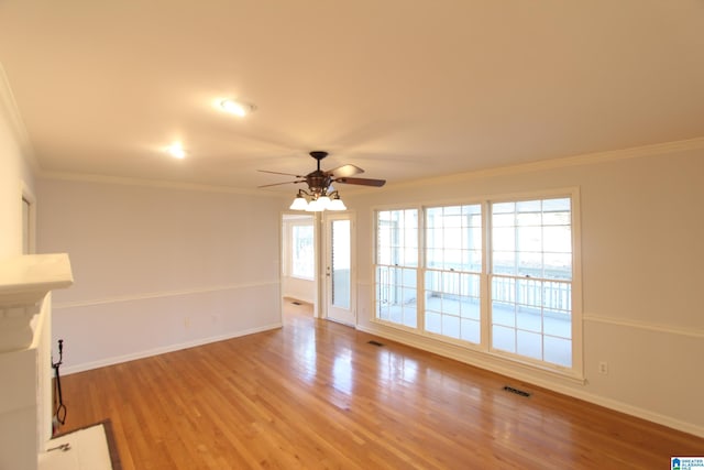 unfurnished living room featuring ceiling fan, wood-type flooring, a wealth of natural light, and ornamental molding