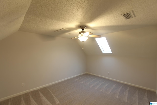 additional living space featuring ceiling fan, vaulted ceiling with skylight, a textured ceiling, and carpet flooring