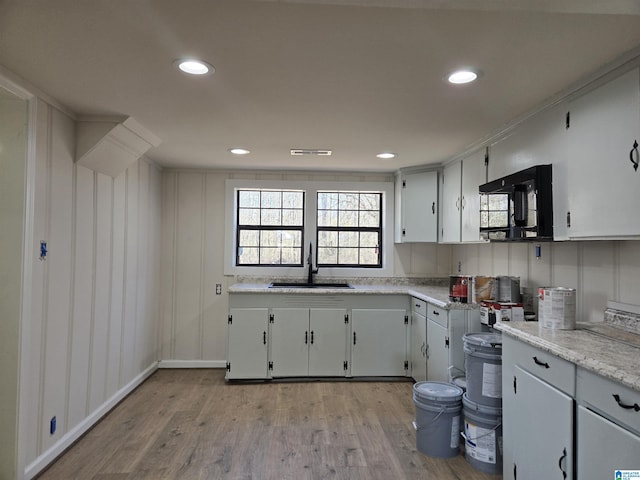 kitchen with white cabinets, light wood-type flooring, sink, and light stone counters