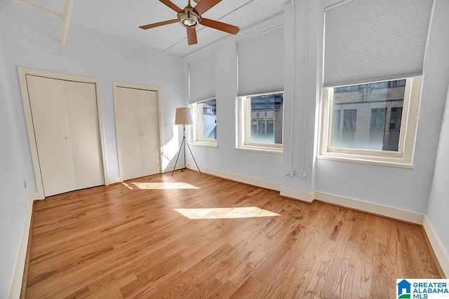 unfurnished bedroom featuring ceiling fan, multiple closets, and light hardwood / wood-style floors