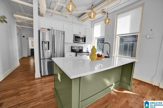 kitchen featuring pendant lighting, white cabinets, stainless steel appliances, light hardwood / wood-style floors, and backsplash