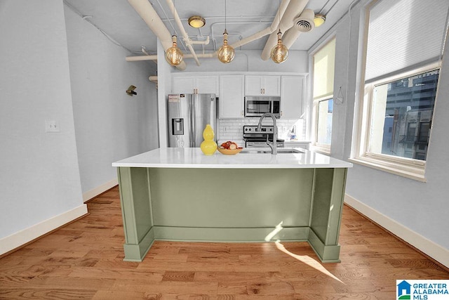 kitchen featuring appliances with stainless steel finishes, white cabinetry, tasteful backsplash, sink, and light wood-type flooring