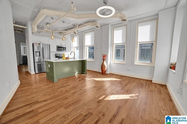 kitchen featuring green cabinets, white cabinetry, light wood-type flooring, a kitchen island with sink, and stainless steel appliances