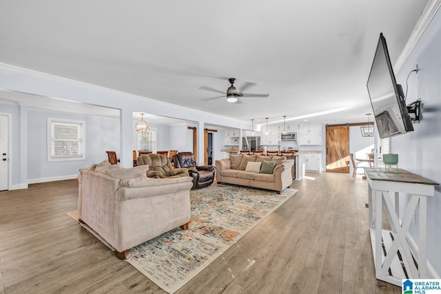 living room with light wood-type flooring, ceiling fan with notable chandelier, ornamental molding, and a barn door