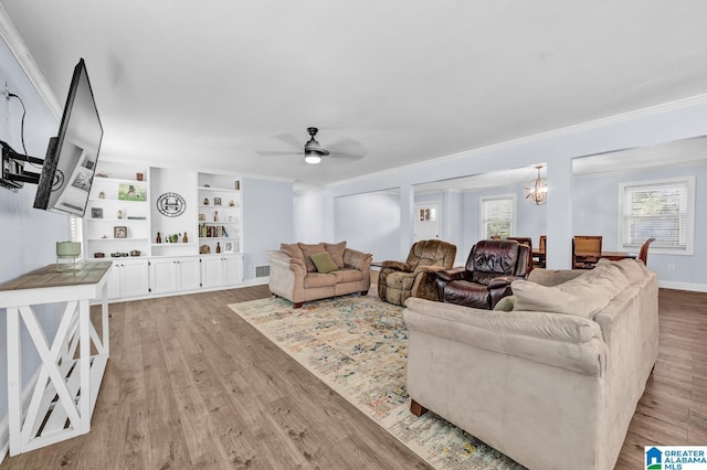 living room with crown molding, light hardwood / wood-style floors, ceiling fan with notable chandelier, and built in shelves