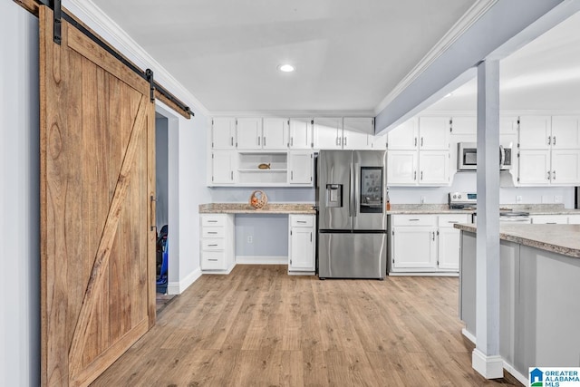 kitchen with a barn door, appliances with stainless steel finishes, white cabinetry, and ornamental molding