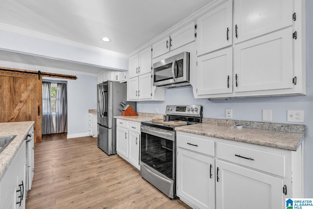 kitchen featuring light hardwood / wood-style floors, a barn door, stainless steel appliances, crown molding, and white cabinets