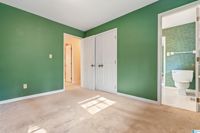 unfurnished bedroom featuring ensuite bathroom, light colored carpet, and a closet