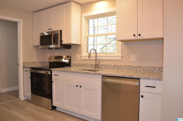 kitchen featuring white cabinetry, appliances with stainless steel finishes, light stone countertops, and sink