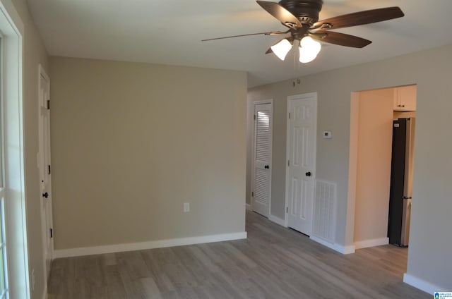 unfurnished bedroom with light hardwood / wood-style floors, stainless steel refrigerator, and ceiling fan