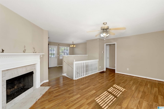 unfurnished living room with ceiling fan with notable chandelier, wood-type flooring, and a fireplace