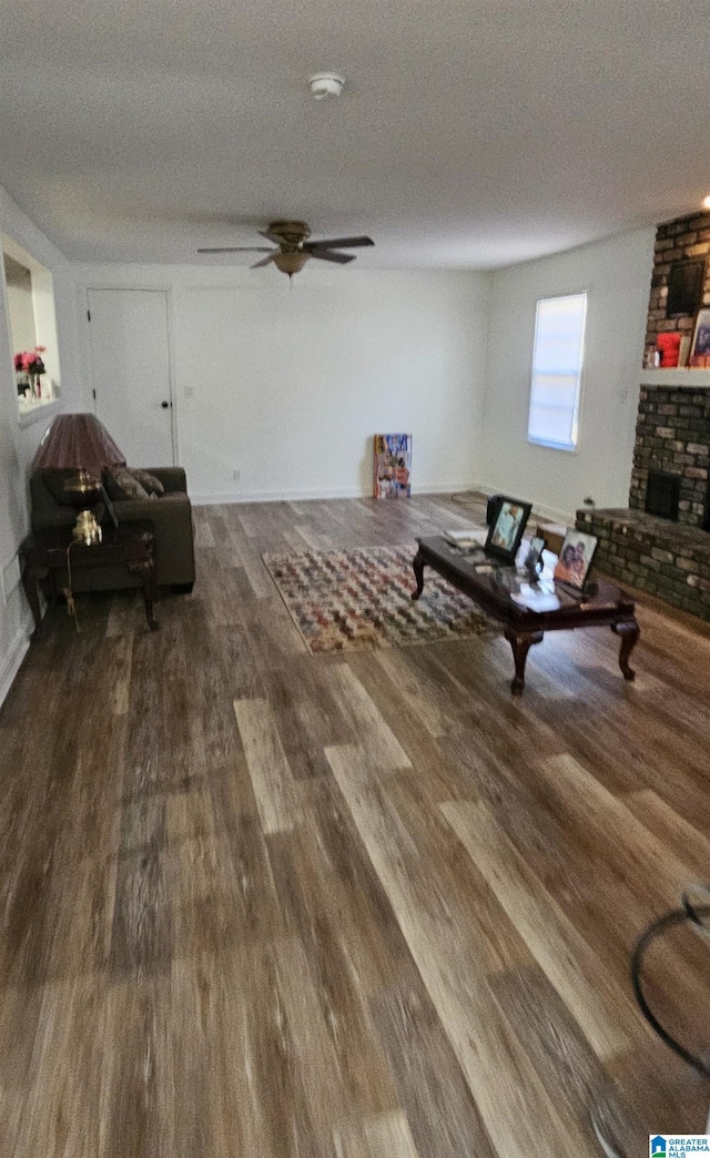 living room featuring ceiling fan, a textured ceiling, dark hardwood / wood-style flooring, and a brick fireplace