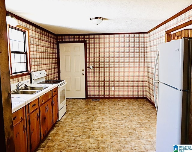 kitchen featuring white appliances, a textured ceiling, sink, tile countertops, and crown molding