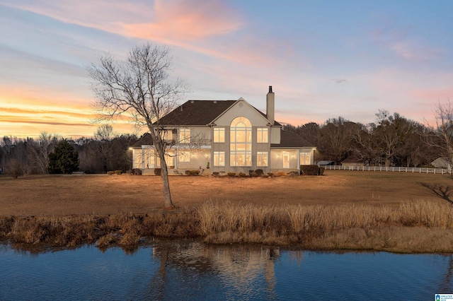 back house at dusk with a lawn and a water view