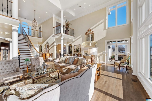 living room featuring a wealth of natural light, crown molding, ornate columns, and a towering ceiling