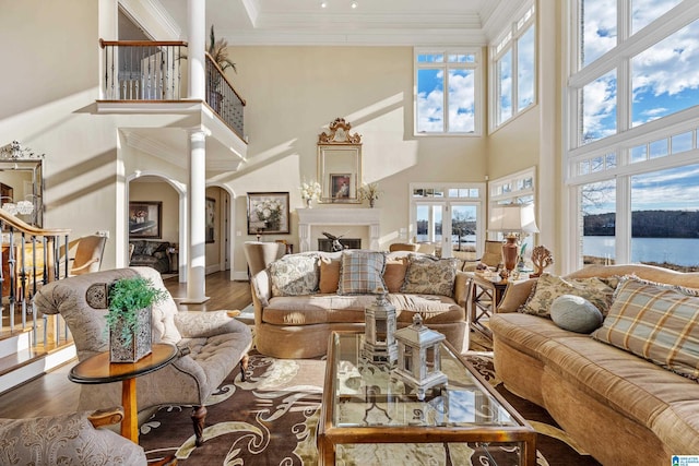 living room with a water view, wood-type flooring, a towering ceiling, and crown molding