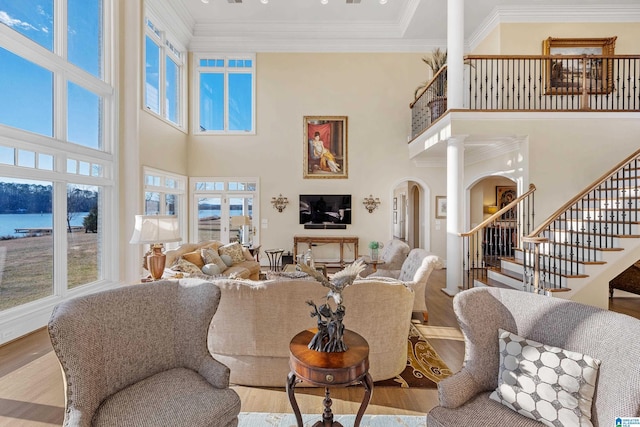 living room with a towering ceiling, ornate columns, a water view, and hardwood / wood-style flooring