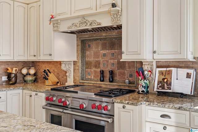 kitchen featuring light stone counters, premium range hood, range with two ovens, and tasteful backsplash