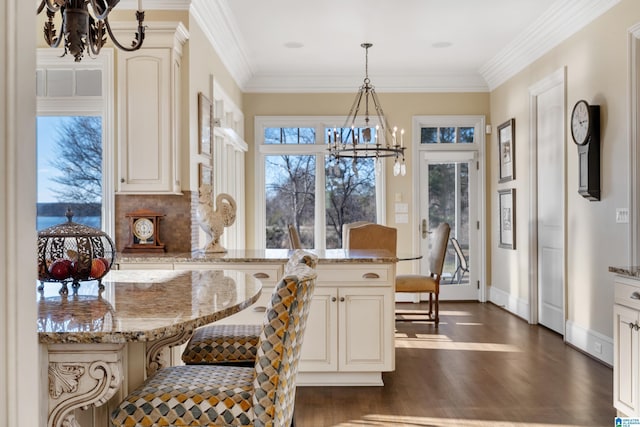 kitchen featuring a breakfast bar area, dark wood-type flooring, hanging light fixtures, light stone countertops, and ornamental molding