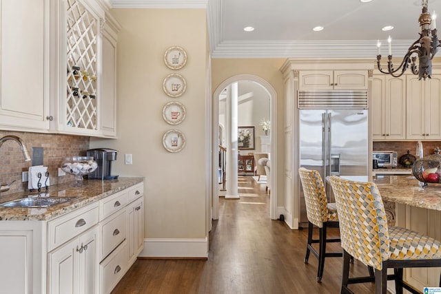 kitchen with tasteful backsplash, light stone counters, sink, and stainless steel built in refrigerator