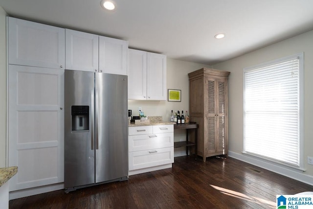 kitchen with stainless steel refrigerator with ice dispenser, dark hardwood / wood-style flooring, white cabinets, a wealth of natural light, and light stone countertops