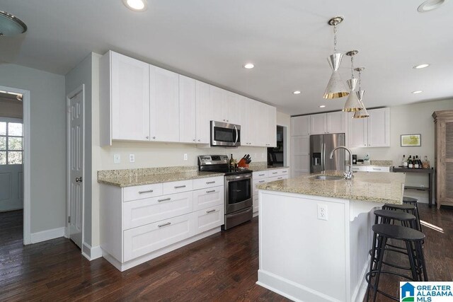 kitchen featuring white cabinets, appliances with stainless steel finishes, an island with sink, sink, and hanging light fixtures