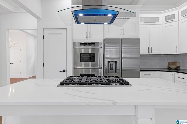 kitchen with dark stone countertops, stainless steel appliances, white cabinets, and island exhaust hood