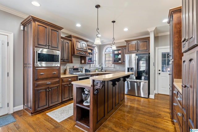 kitchen featuring appliances with stainless steel finishes, hanging light fixtures, a kitchen island, dark brown cabinetry, and sink