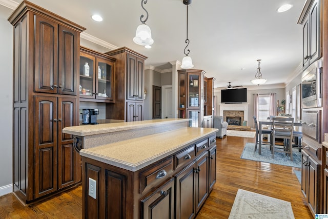 kitchen featuring pendant lighting, a center island, a stone fireplace, dark hardwood / wood-style floors, and dark brown cabinets