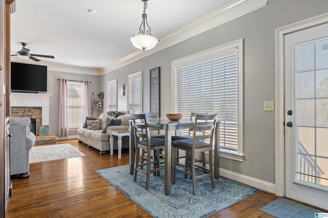 dining space featuring ceiling fan, dark hardwood / wood-style flooring, ornamental molding, and a fireplace