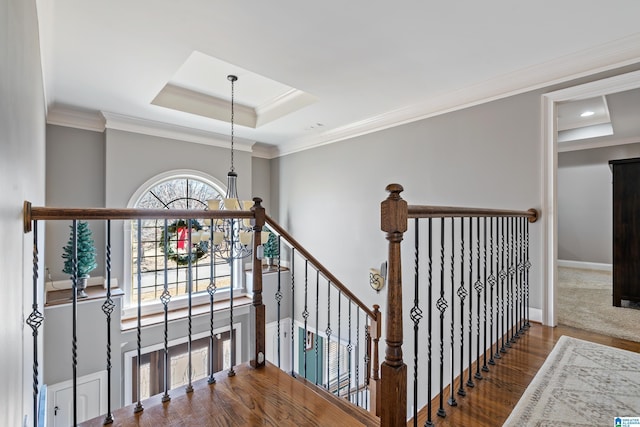 stairway featuring hardwood / wood-style flooring, a tray ceiling, crown molding, and a notable chandelier