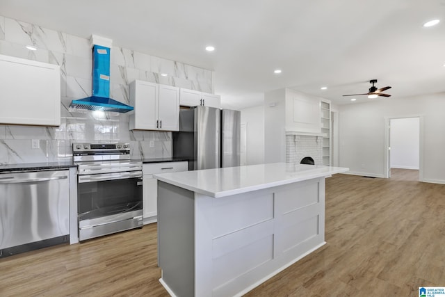 kitchen with ventilation hood, appliances with stainless steel finishes, light hardwood / wood-style floors, decorative backsplash, and white cabinets