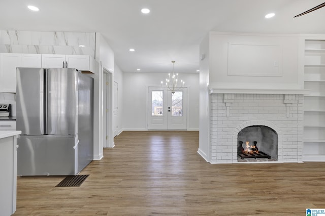 kitchen featuring light hardwood / wood-style flooring, stainless steel refrigerator, pendant lighting, a fireplace, and white cabinets