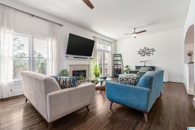 living room with ceiling fan, a wealth of natural light, dark hardwood / wood-style flooring, and a premium fireplace