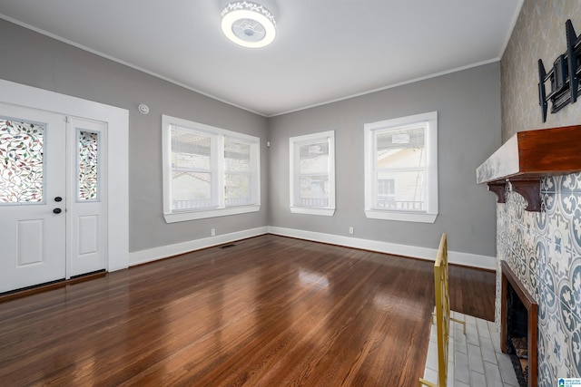 entrance foyer with dark wood-type flooring, a tile fireplace, crown molding, and plenty of natural light