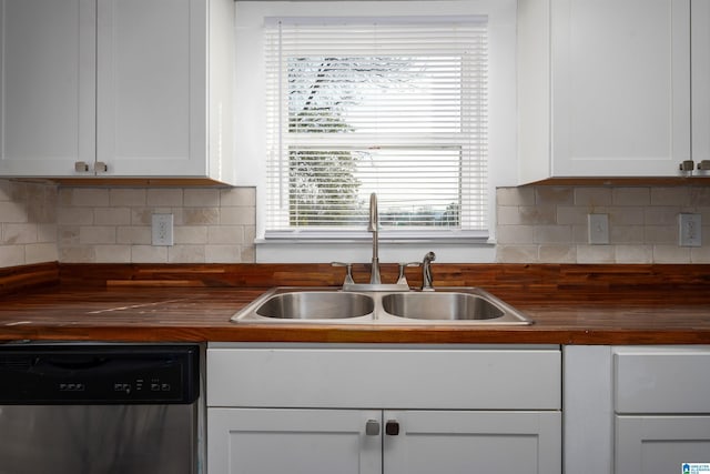 kitchen with stainless steel dishwasher, white cabinets, wooden counters, and sink