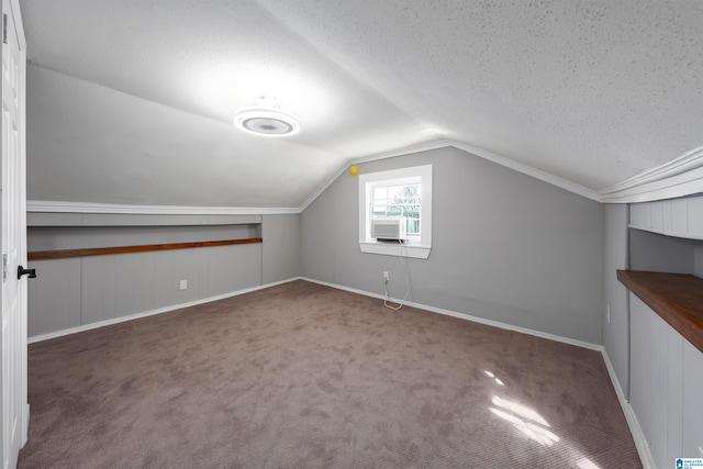 additional living space featuring a textured ceiling, lofted ceiling, and dark colored carpet