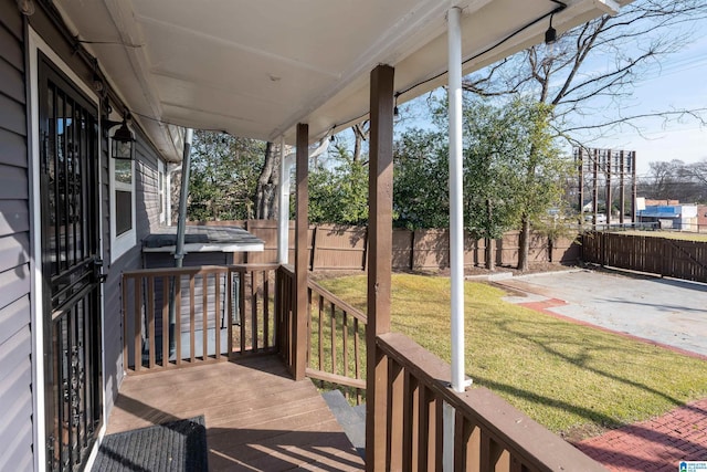 deck featuring a hot tub, a lawn, and a patio