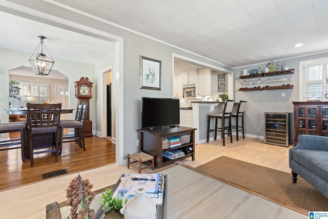 living room with crown molding, light hardwood / wood-style floors, wine cooler, and a notable chandelier