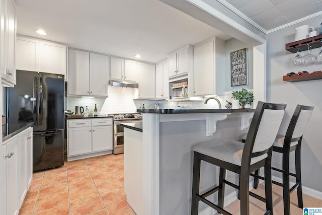 kitchen with kitchen peninsula, white cabinets, tasteful backsplash, a breakfast bar, and stainless steel appliances