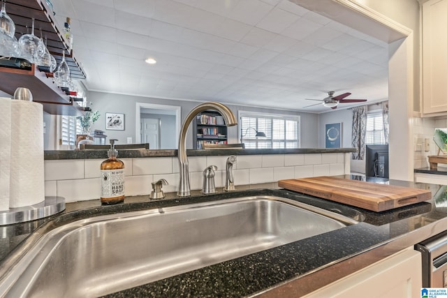 kitchen featuring ceiling fan, white cabinetry, sink, ornamental molding, and backsplash