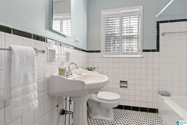 bathroom with toilet, a wealth of natural light, tile walls, and tile patterned flooring