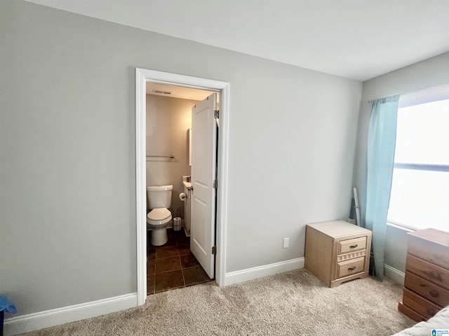 bedroom with ensuite bathroom and dark colored carpet