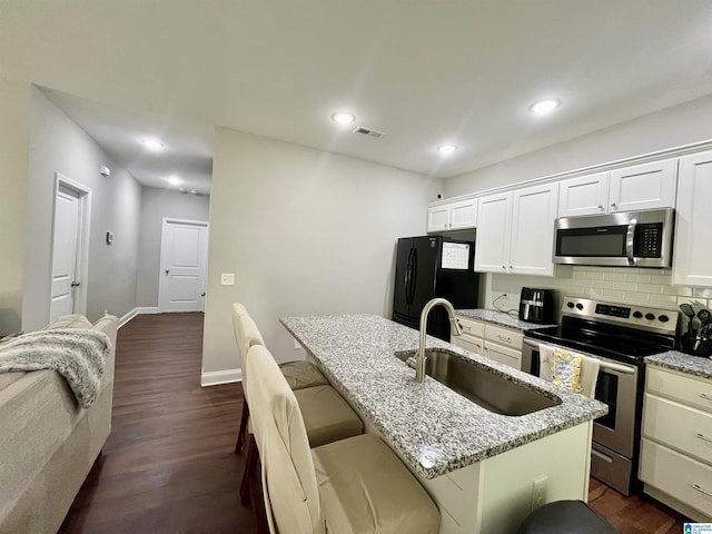 kitchen featuring white cabinets, stainless steel appliances, sink, a kitchen island with sink, and light stone counters